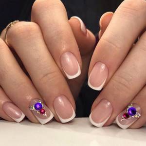 Classic French on short nails using large colored rhinestones and small rhinestones.