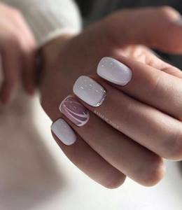 Короткие квадратные ногти покрыты белым лаком, с акцентом на среднем пальчике в виде серебряной лунки, и красивый рисунок на безымянном пальчикке на прозрачной основе.